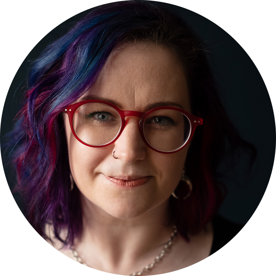 Michelle O'Conor, a white woman with purple and blue hair wearing red glasses.
