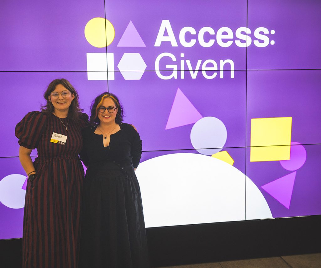 Ellen and Michelle stand in front of a big screen with purple graphics and the wording "Access Given" they are smiling.